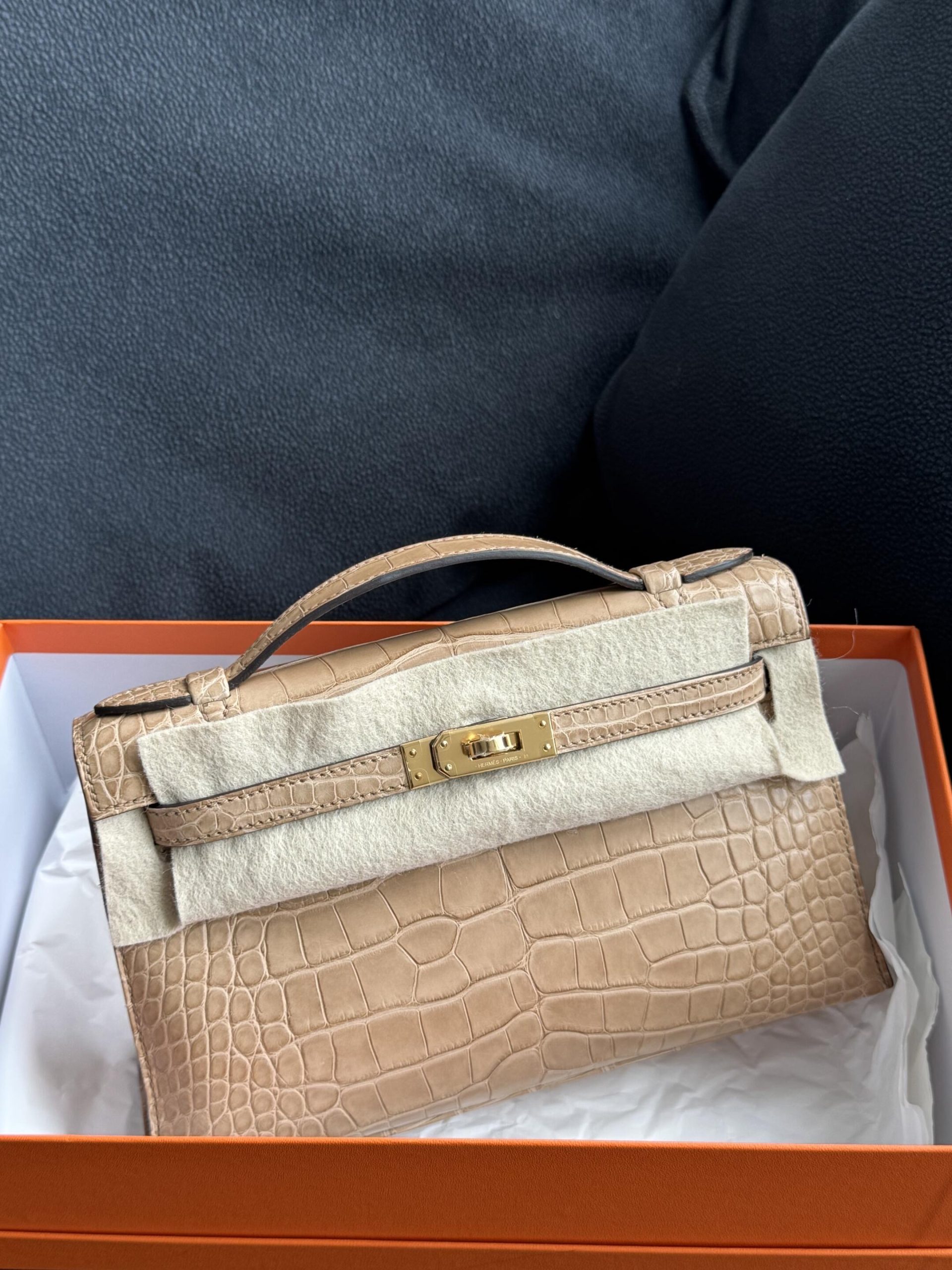 Unboxing of a brand new Hermès Kelly Pochette clutch in matte beige alligator leather inside its signature orange box.