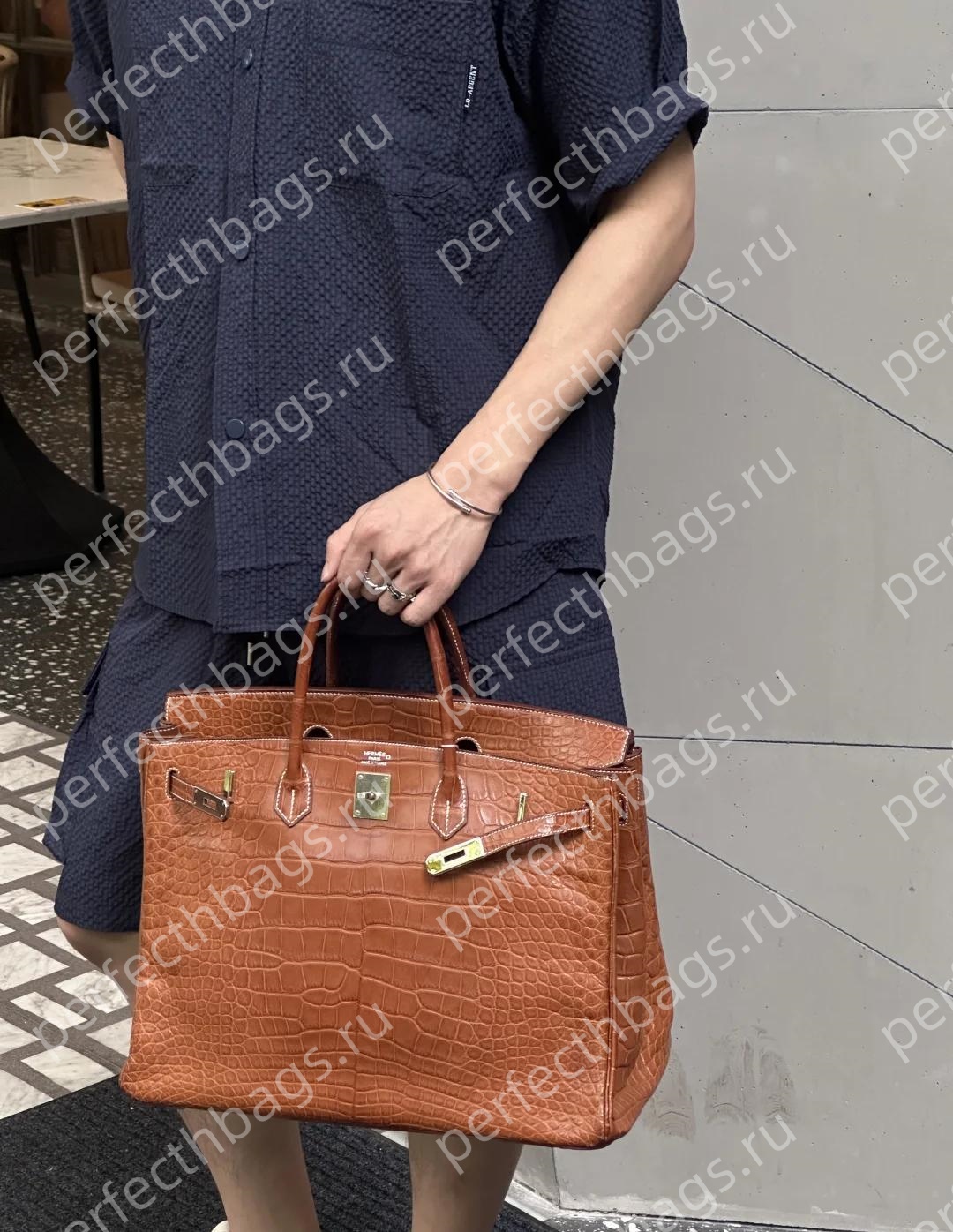Matte brown Birkin bag crocodile leather carried by a client, luxury handmade craftsmanship.