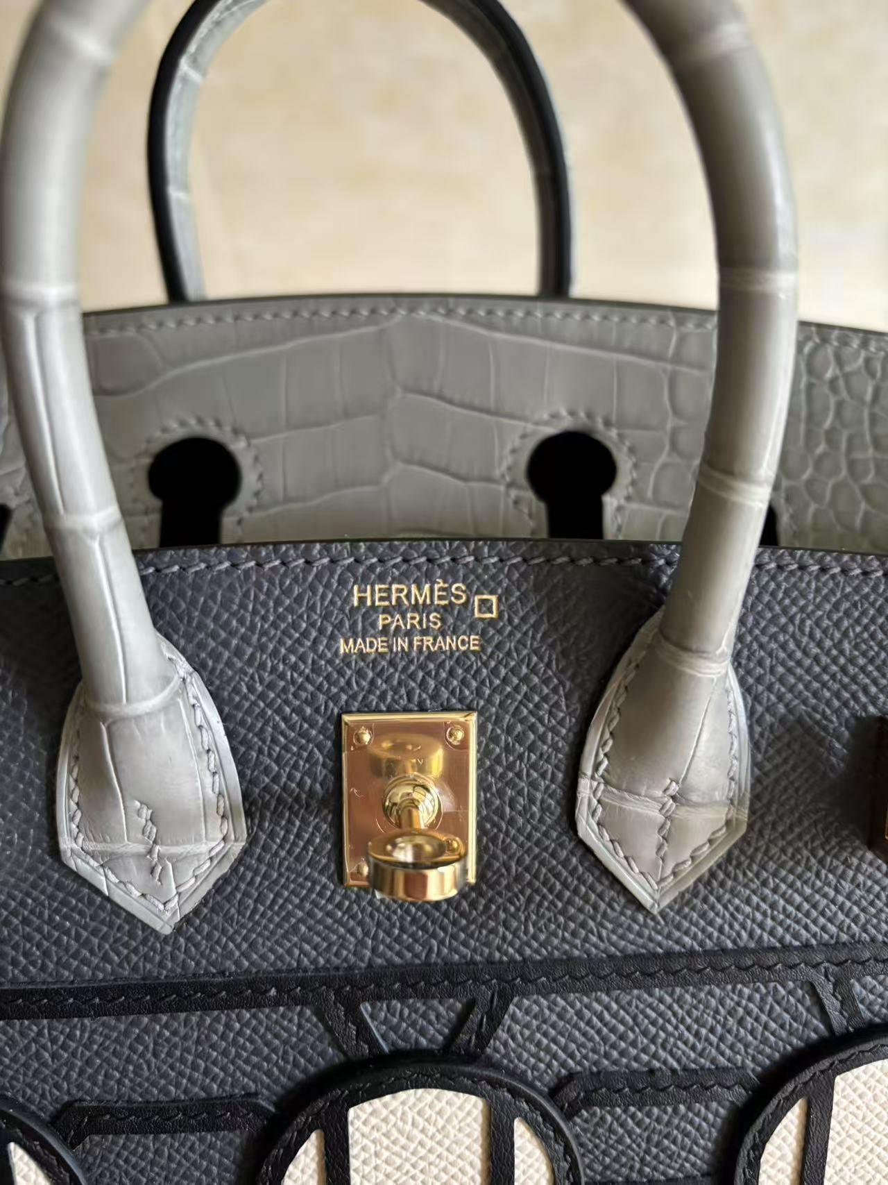 Close-up detail of the "HERMÈS PARIS MADE IN FRANCE" gold foil stamp on a Birkin Faubourg bag with exotic alligator leather handles.