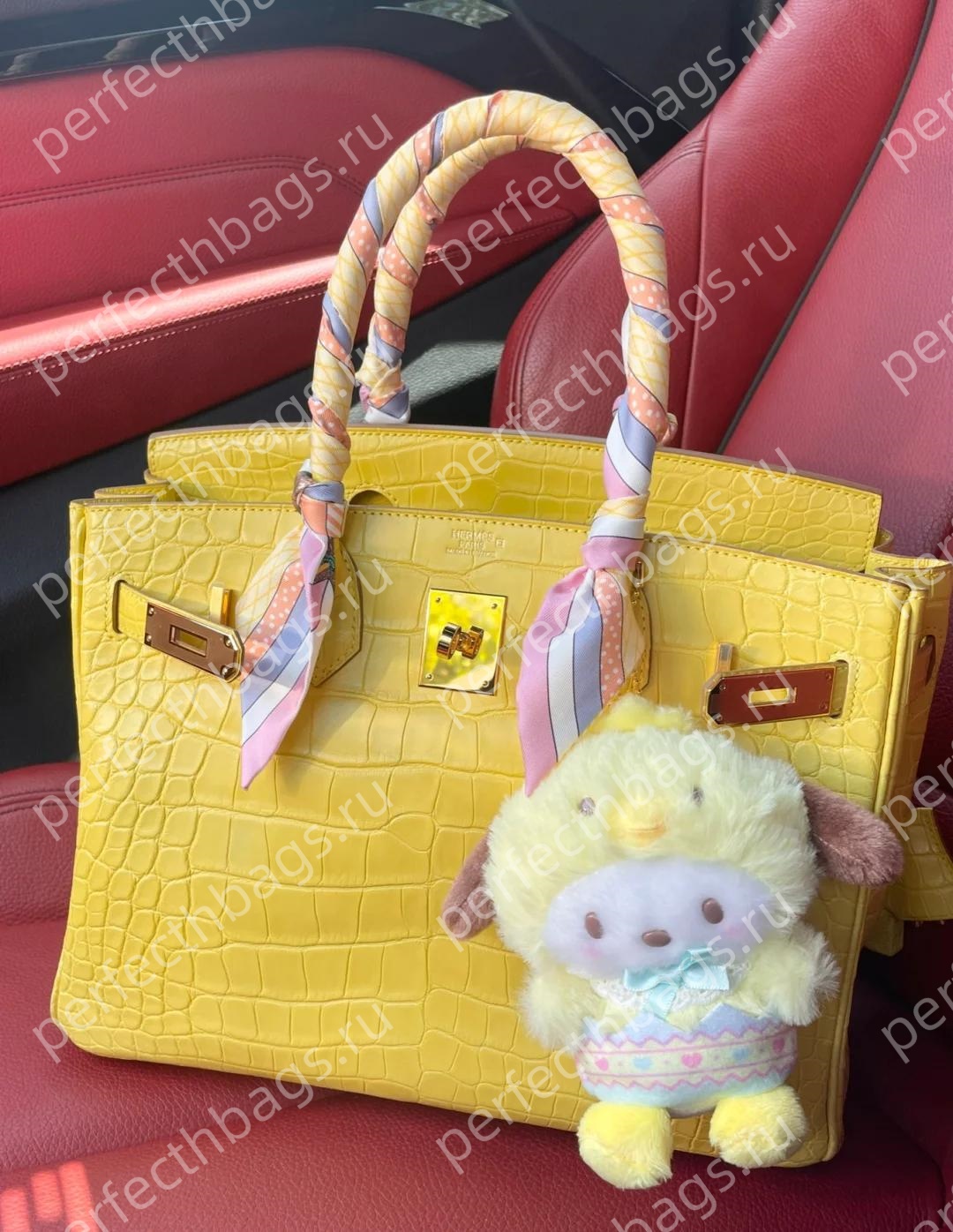 Bright yellow Hermes crocodile Birkin bag with twilly and charm inside a luxury car, exotic leather collection.