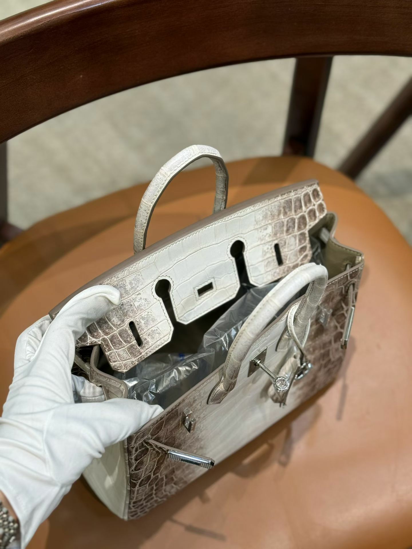 A gloved hand holds the handles of an open Himalayan Diamond Birkin