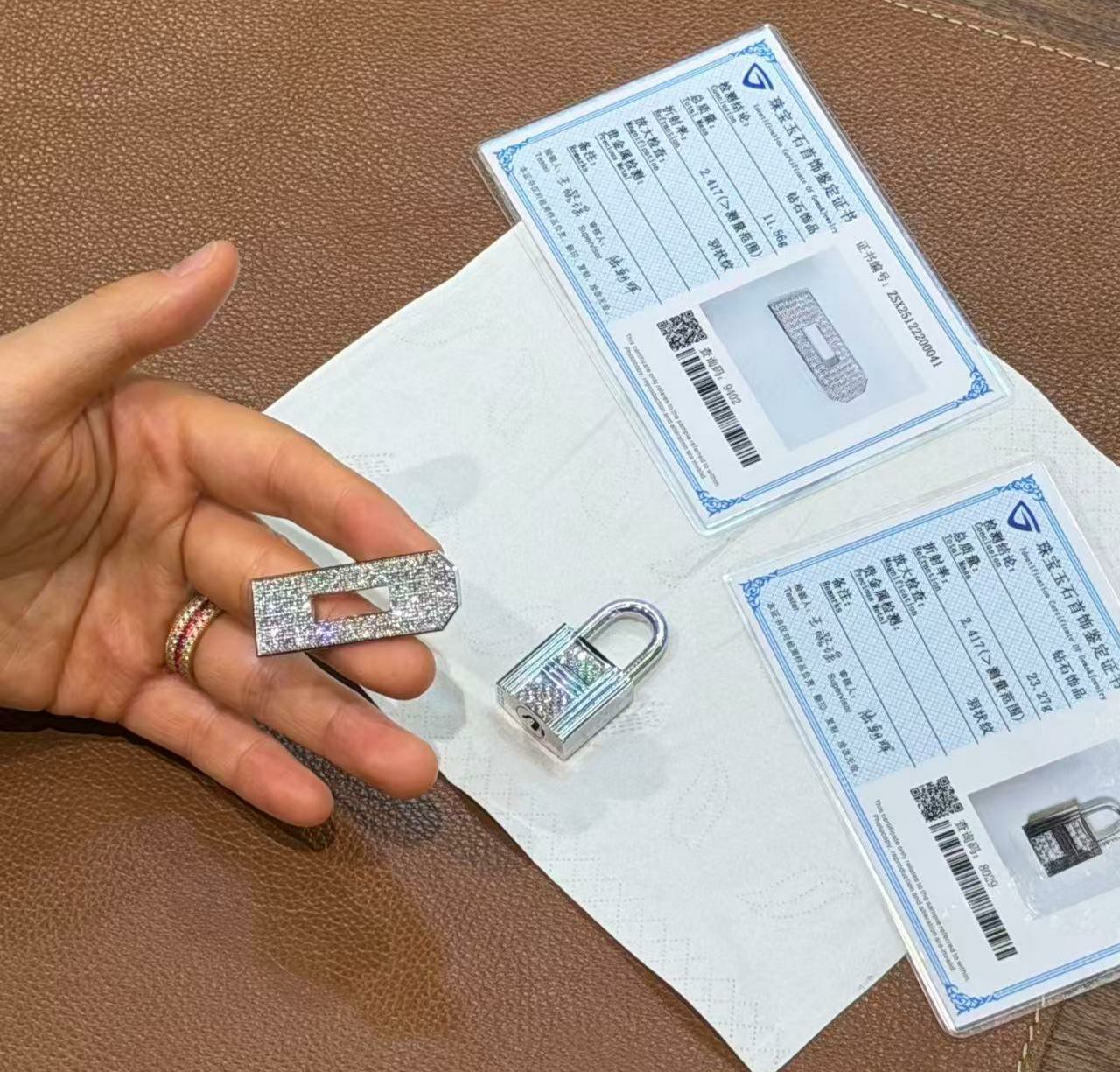 A close-up of jewelry-grade identification certificates alongside custom 18k white gold and diamond hardware for a Himalayan Birkin 25