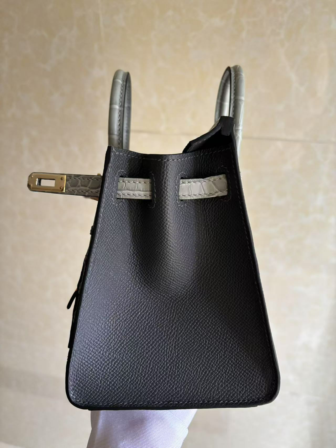 A focused view on the left hardware of the Faubourg Birkin Rainy Day, featuring the gold-plated plaque and the matte alligator strap against the Epsom body.