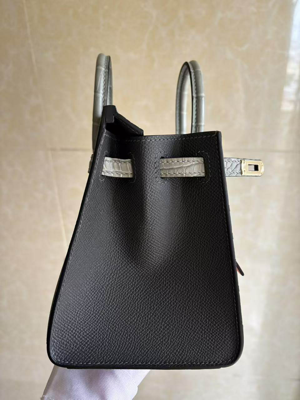 A focused view on the right hardware of the Faubourg Birkin Rainy Day, highlighting the precision of the stitching on the alligator strap and the structured side gusset.