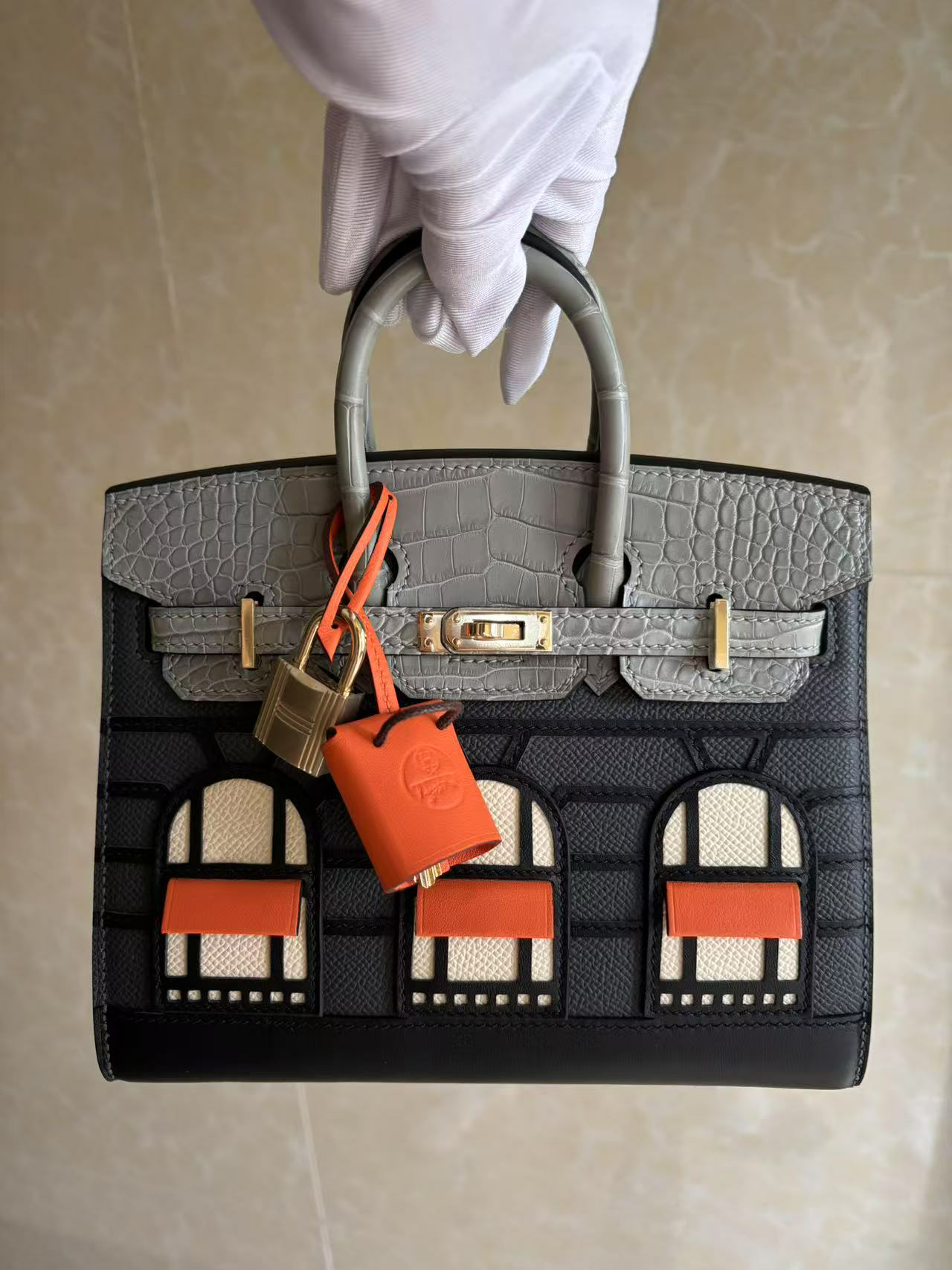 The front of the Hermes Faubourg Birkin Rainy Day shown with its accessories attached: the padlock and the orange 'shopping bag' clochette.