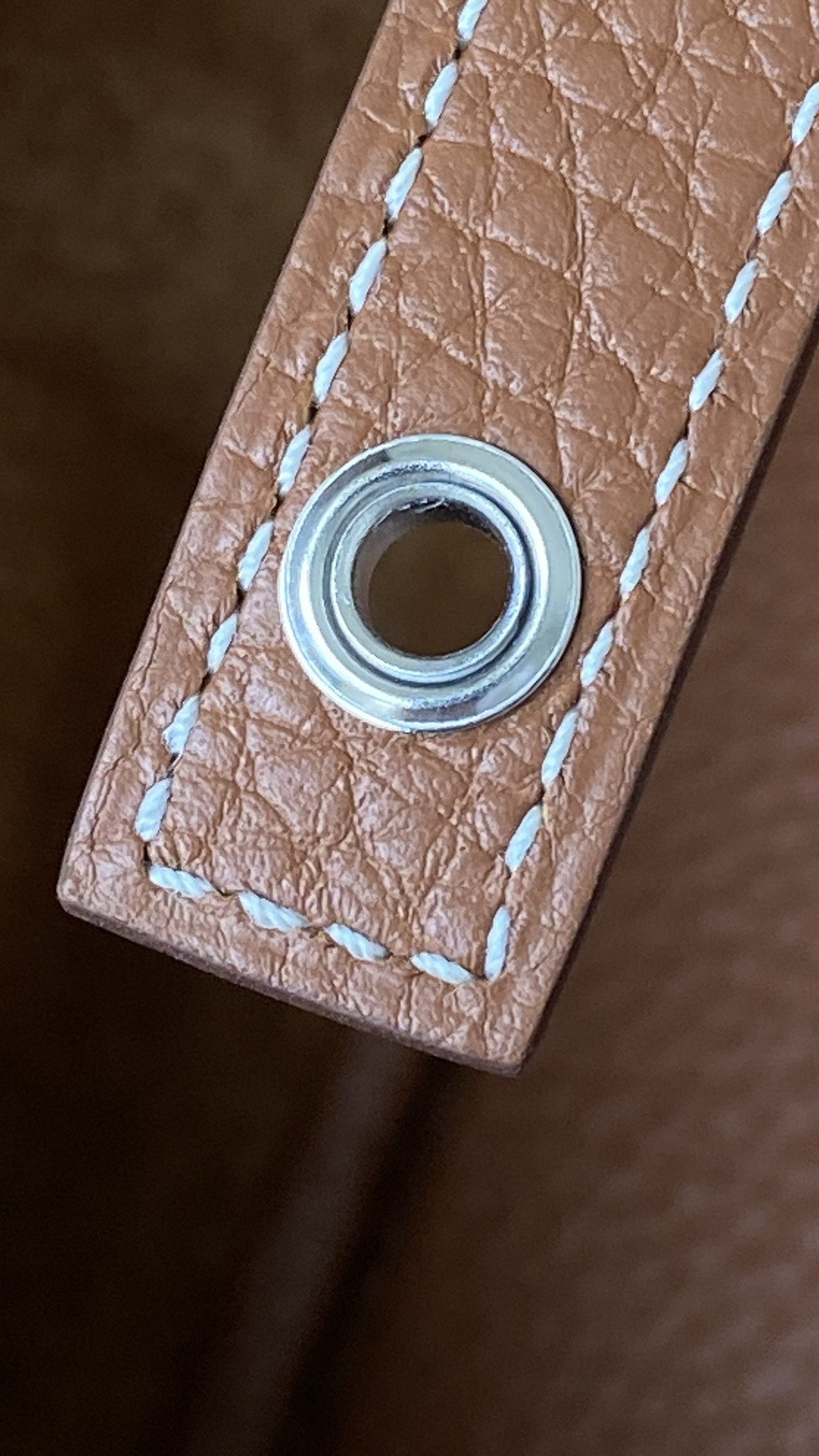 An extreme close-up view of the Hermes Picotin bag, showcasing the polished silver-toned metal eyelet, the precise saddle stitching with white thread, and the fine grain of the gold-colored Clemence leather.