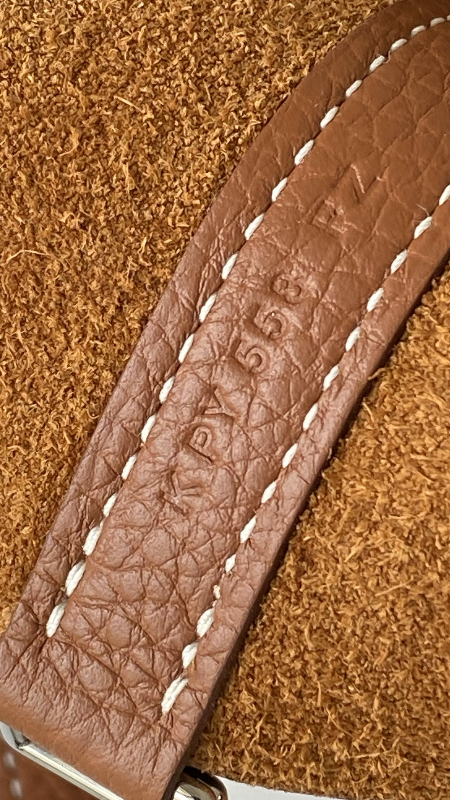 Macro close-up of a stamped serial number on a Picotin bag handle strap against raw suede background.