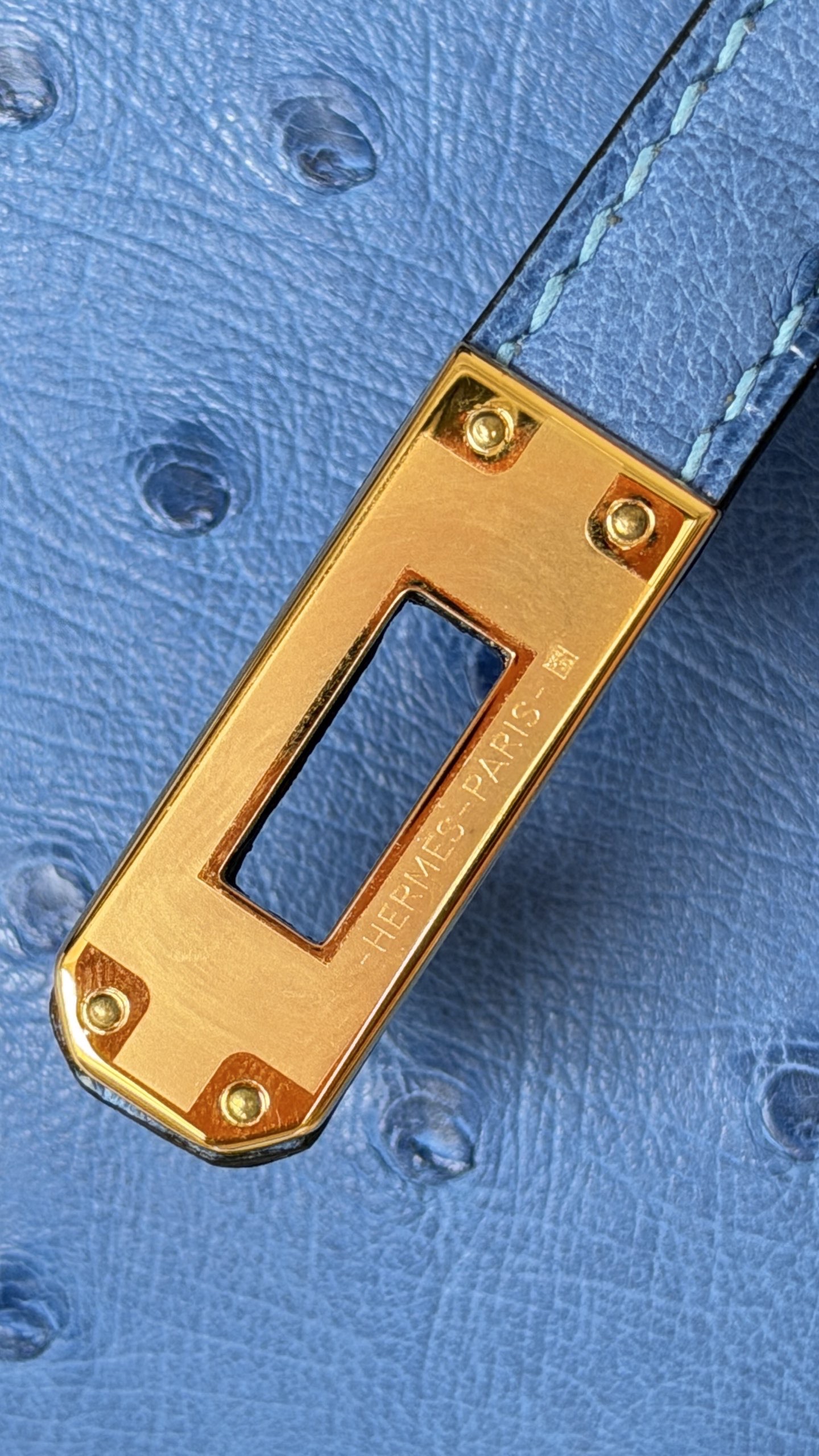 Close-up of the 'HERMÈS PARIS' stamping on the hardware of a blue ostrich hermes kelly pochette.