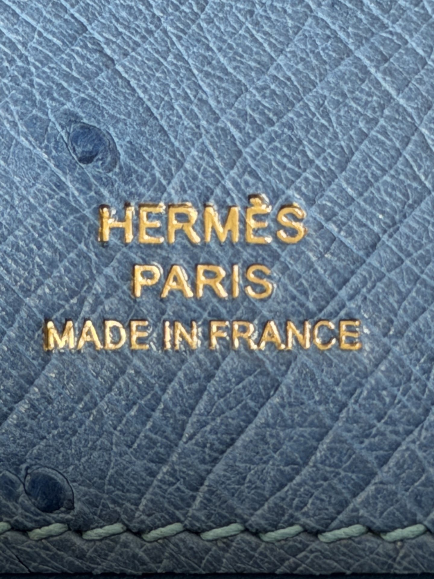 Close-up of the heat stamp on a hermes kelly pochette in blue ostrich leather.