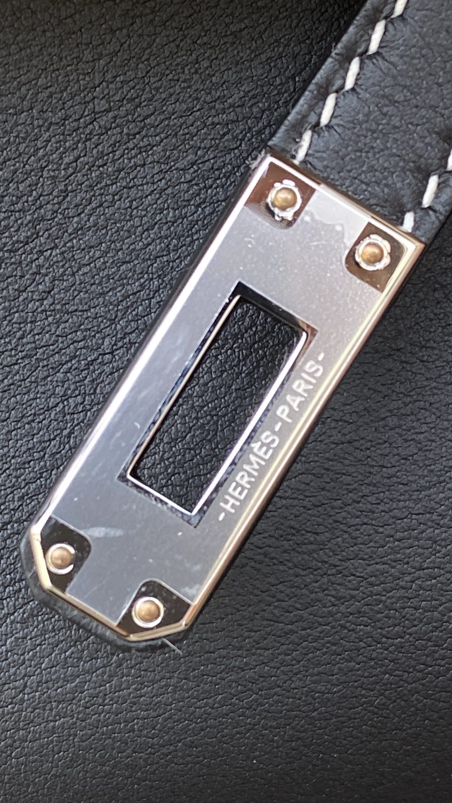 Macro shot of the palladium hardware on the Hermès Kelly Pochette, showing the manual pearling technique on the rivets.