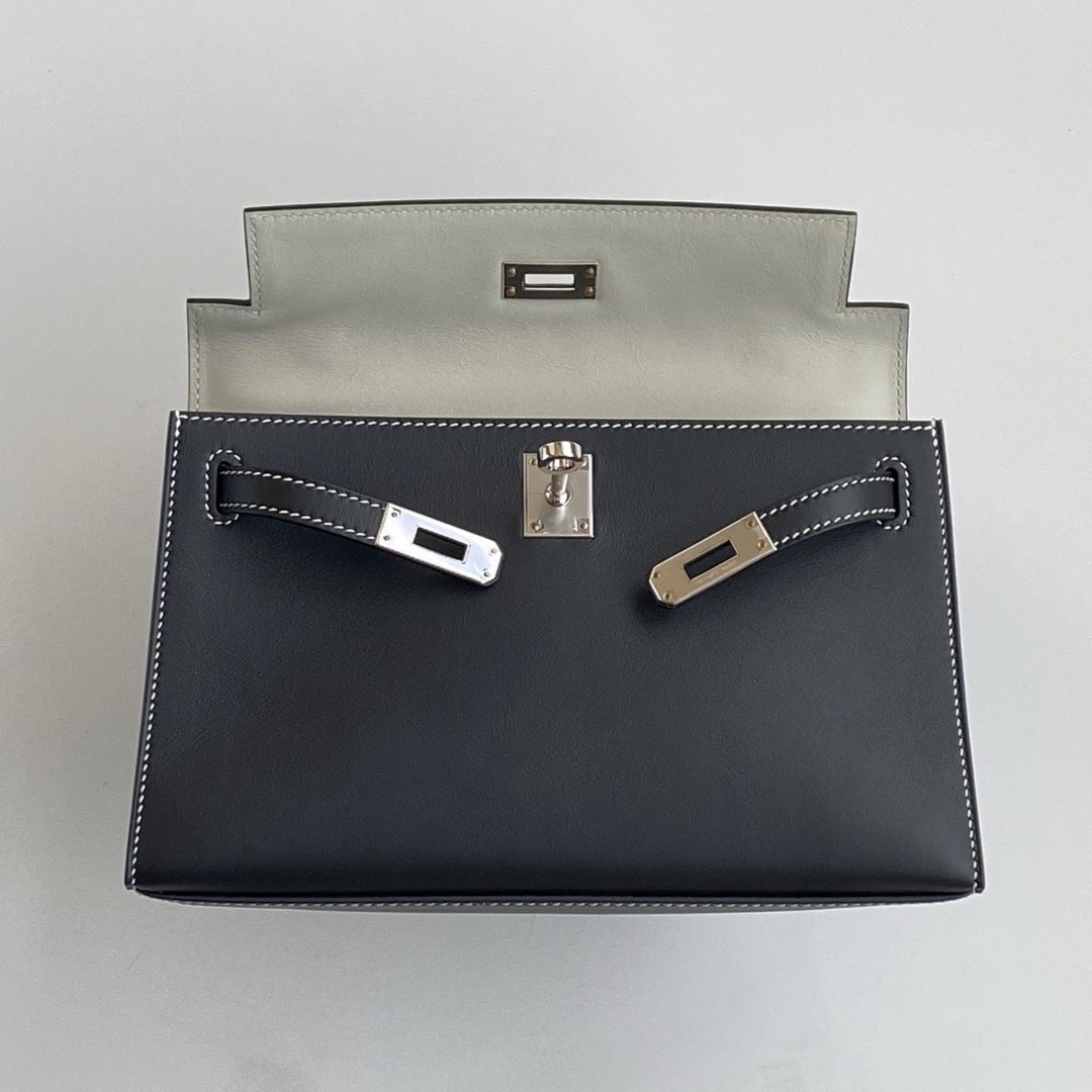 Open view of the Hermès Kelly Pochette clutch, revealing the contrasting Gris Perle interior lining against the black Swift exterior.