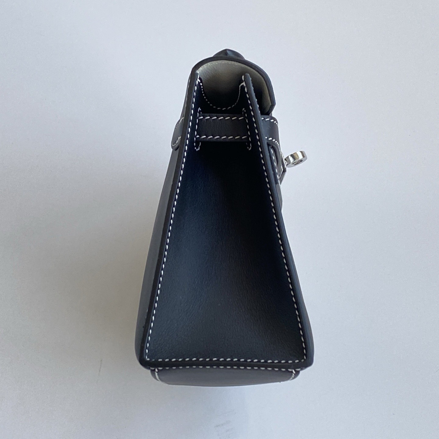 Side profile of the structurally perfect Hermès Kelly Pochette, showing the neat side stitching on black Swift leather.