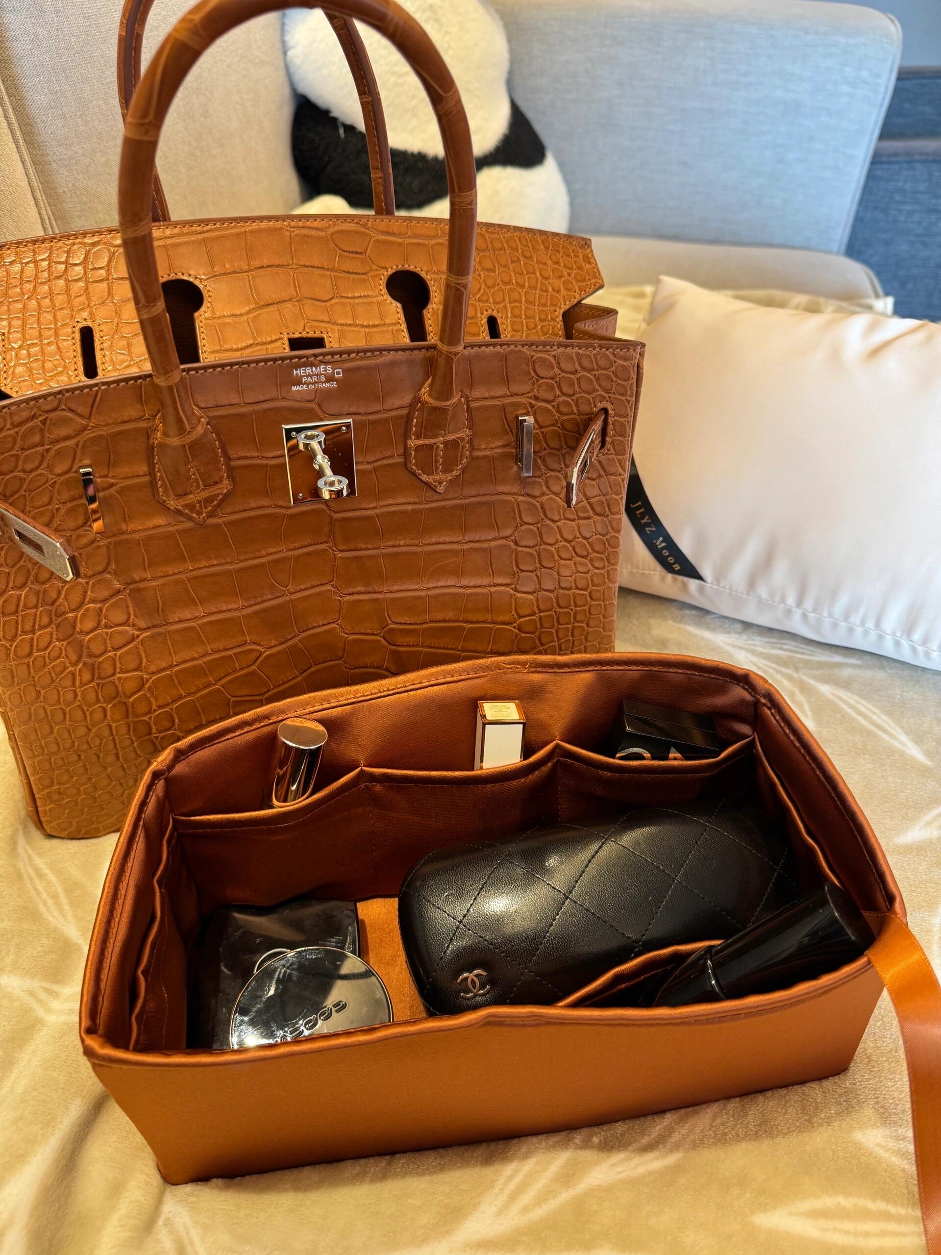 A gold-brown Hermès Birkin alligator bag shown open with a satin bag organizer insert filled with cosmetics, highlighting the birkin bag alligator interior space.