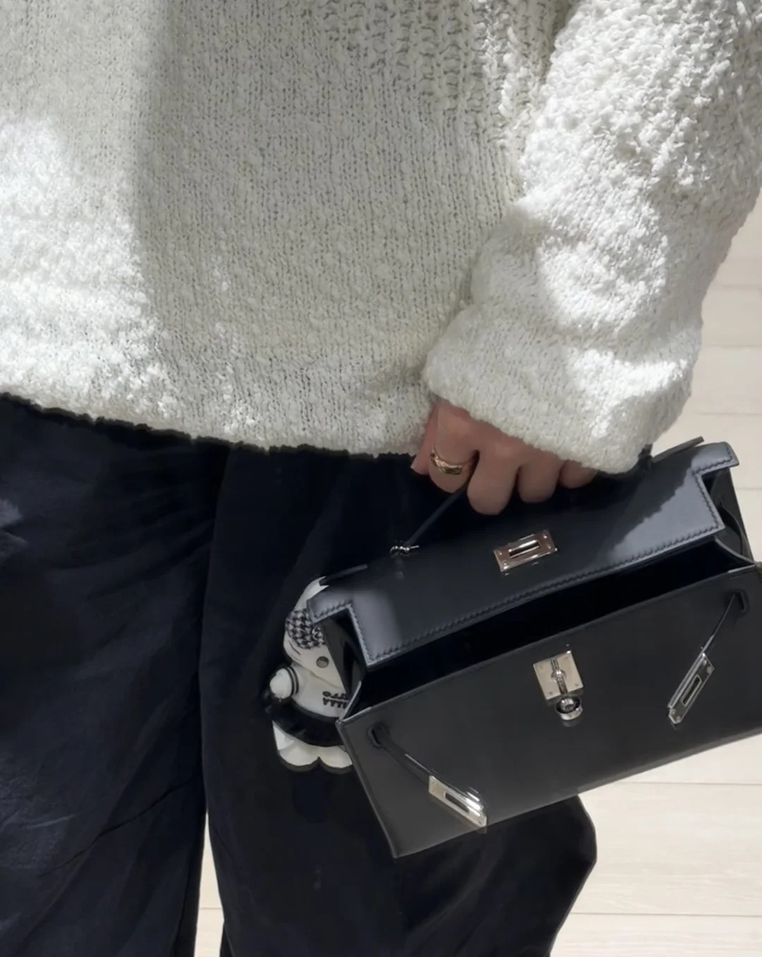 A buyer carrying a black leather Hermès Kelly Pochette clutch bag slightly open, showing the spacious interior structure.