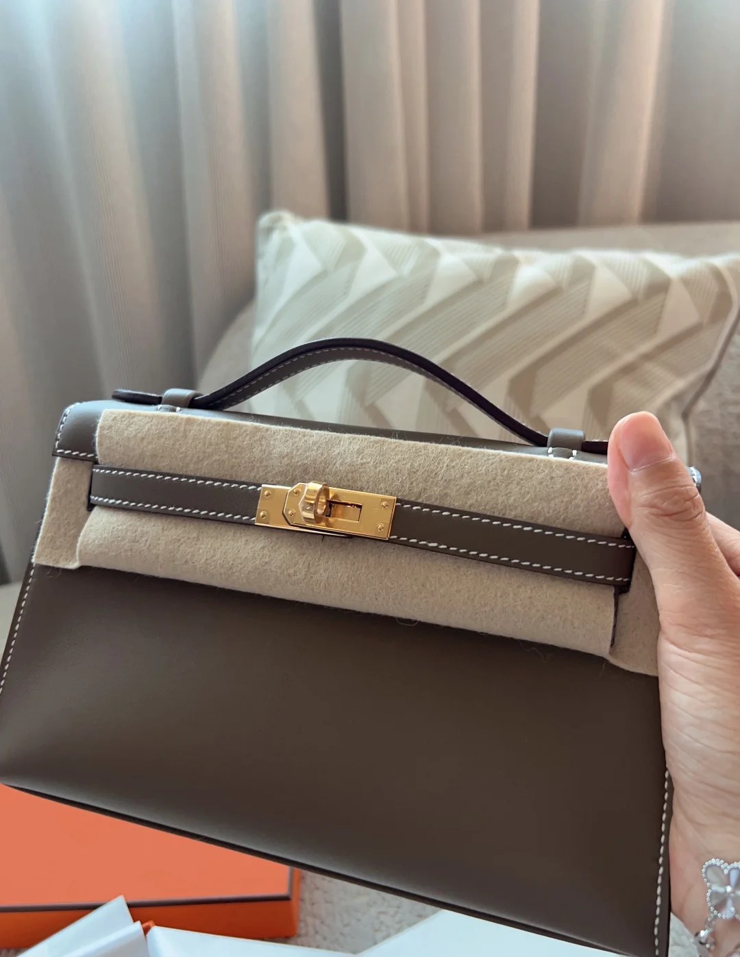 Handheld view of an Hermès Kelly Pochette clutch in etoupe grey smooth leather