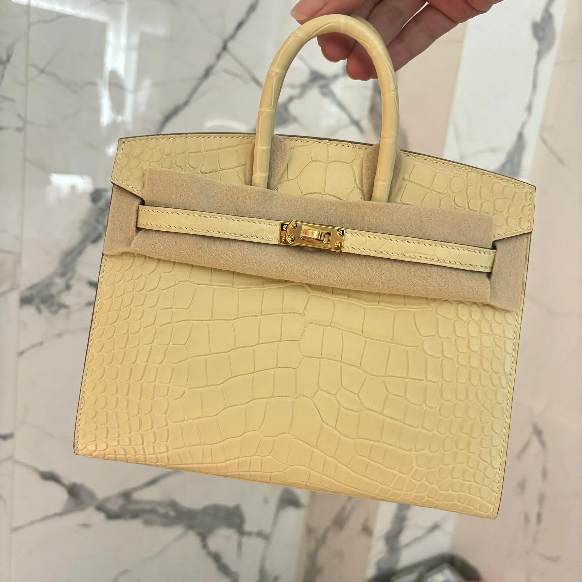 A luxury light yellow Hermès Birkin alligator bag held by hand