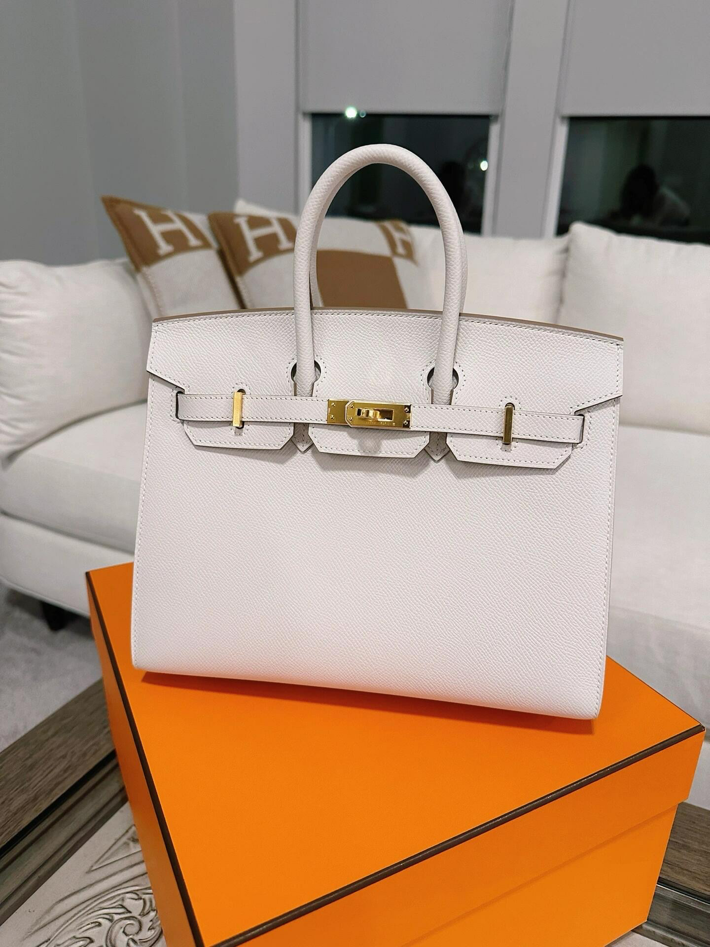 A high-end white Birkin bag with gold hardware (GHW) displayed on its orange luxury box